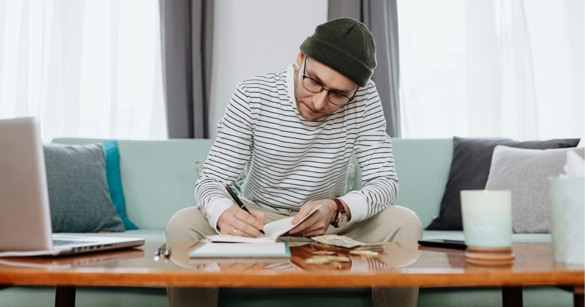 Person writing budget goals in a colorful notebook at a bright clean desk