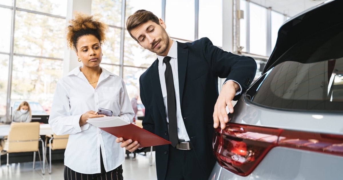 Two people reviewing car purchase paperwork across a table in a calm well-lit setting