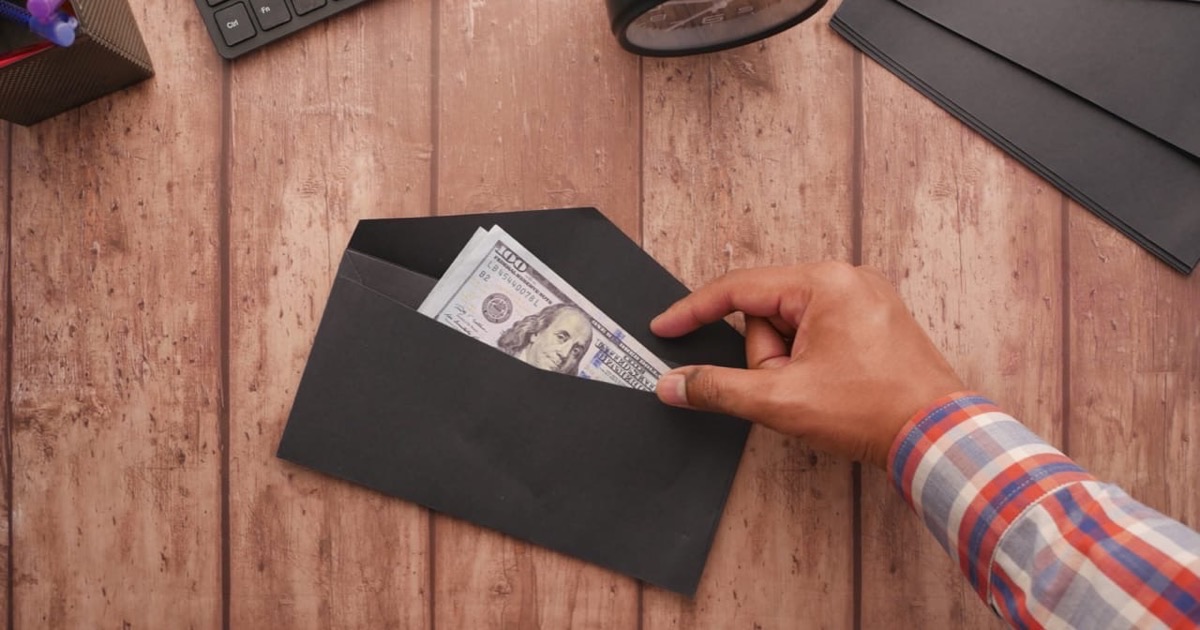 Person sorting labeled cash envelopes and paper bills at a clean bright desk